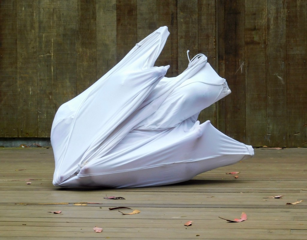 A crumpled fabric and pipe cube sculpture that now looks like an odd sort of bird wings upstretched leaning on its side.