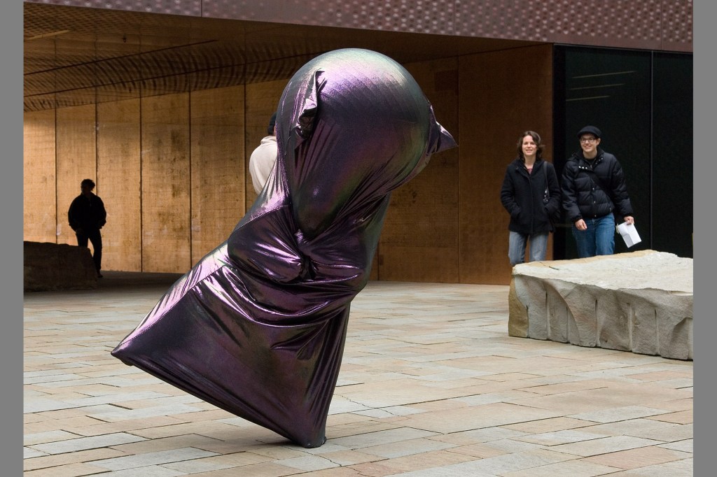 A living sculpture made from a human and a large ball inside an iridescent stretchy sheath dances in the courtyard outside the de Young Museum.