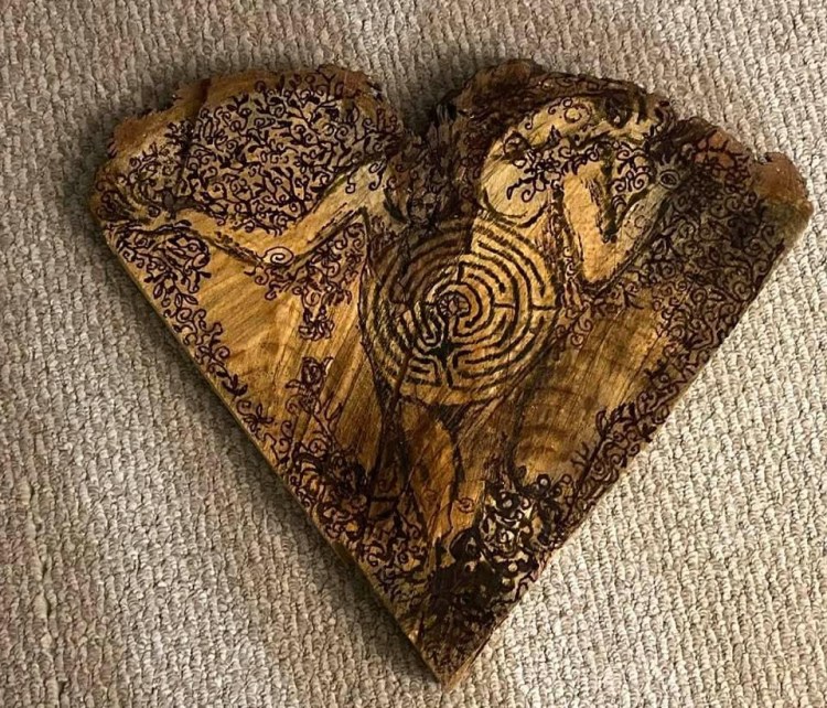 Roughly heart shaped wood slice with a tree woman drawn on it.
