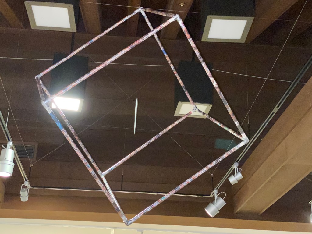 Hanging PVC cube covered in eyes with a labyrinth hand hanging inside at the center.