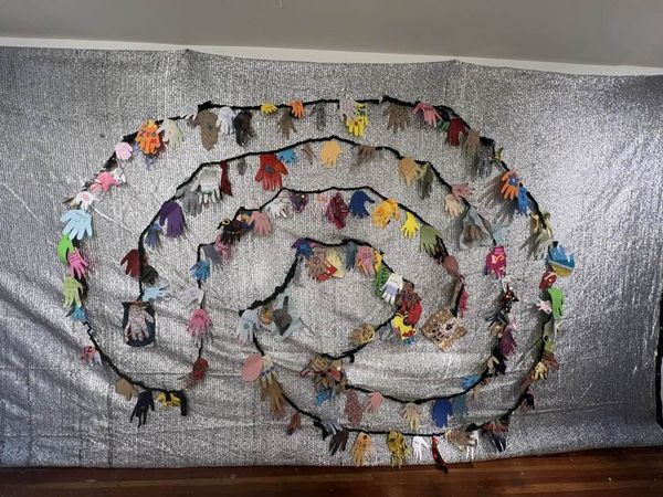 Three circuit labyrinth made from twisted fabric with colorful hands attached sewn to a silvery mesh background.